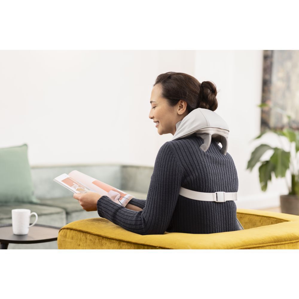 Femme assise sur un canapé, masseur de cou. Appareil gris avec sangles. Femme se détend.