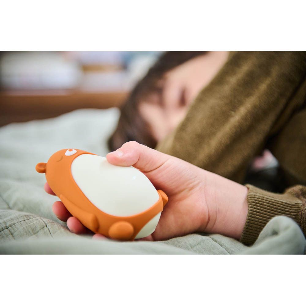Moonbird Moonbuddy Barry l'ours, orange et blanc, tenu dans une main. Personne allongée.