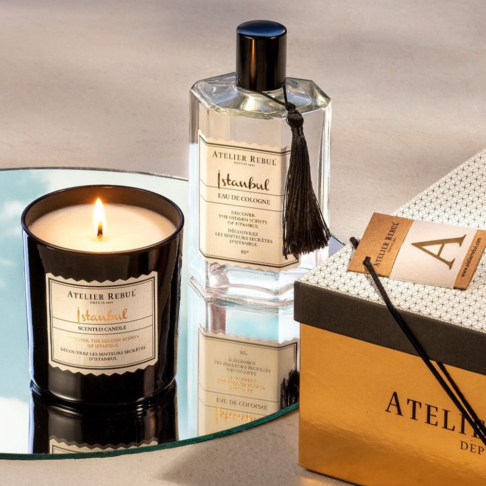 Brennende Duftkerze und Eau de Cologne auf einem Spiegel, neben einer Geschenkbox.