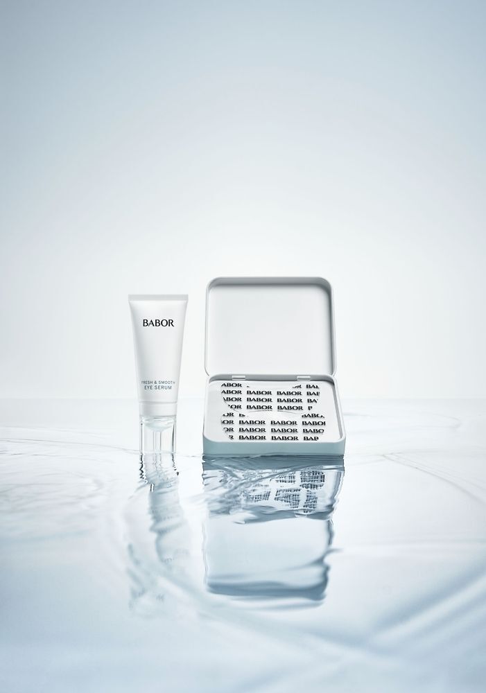 Eine Tube Serum und eine geöffnete Dose mit Augenpatches. Auf Wasser. Auf der Tube steht BABOR.