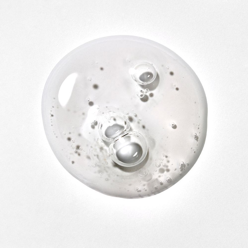 Nahaufnahme einer klaren Flüssigkeit mit Blasen. Die Flüssigkeit ist auf einer weißen Oberfläche verteilt.