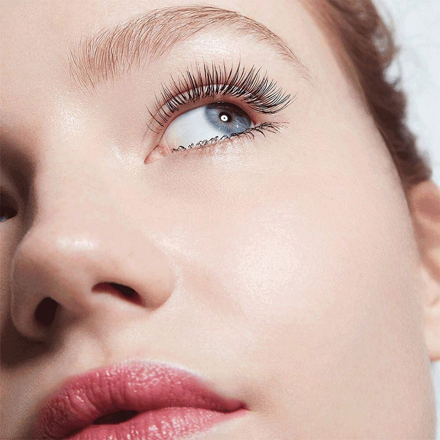 Nahaufnahme eines Gesichts mit langen, getuschten Wimpern. Roter Lippenstift. Blick nach oben.