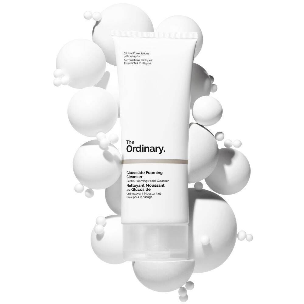 Eine Tube The Ordinary Glucoside Foaming Cleanser umgeben von weißen Kugeln.