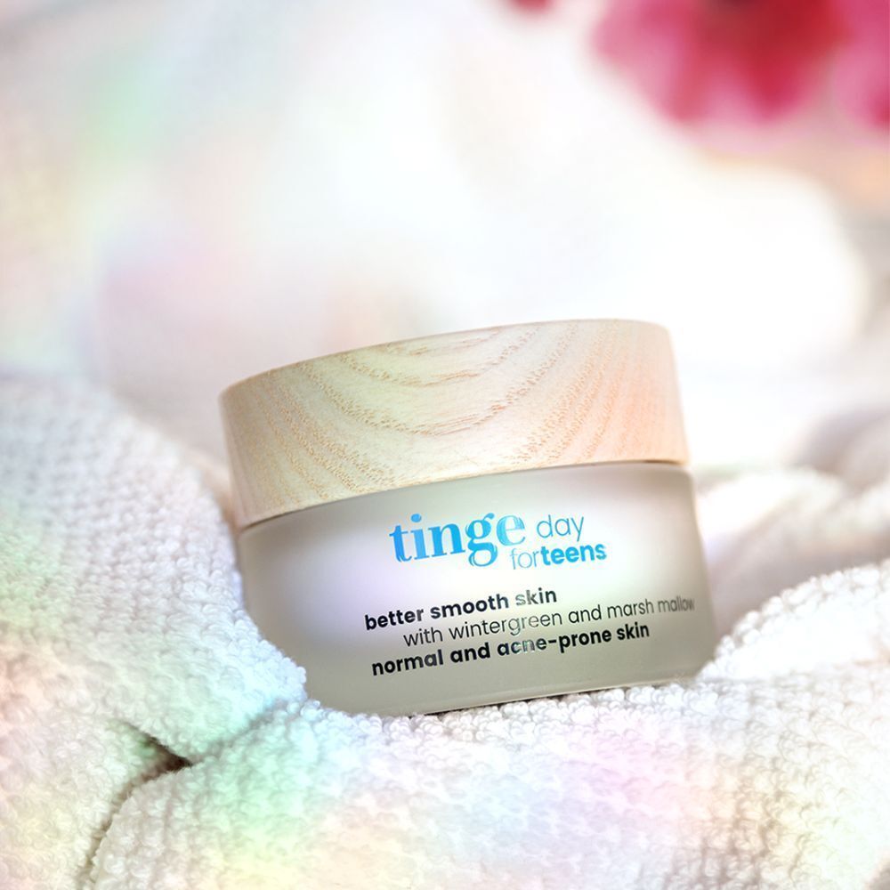Ein Tiegel mit hellem Holzdeckel auf weißem Handtuch. Aufschrift: Tinge day for teens, better smooth skin, mit Wintergrün und Eibisch, für normale und zu Akne neigende Haut.