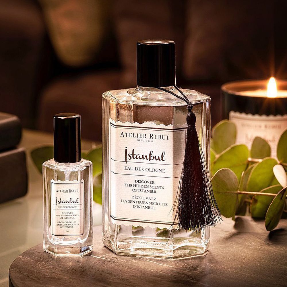 Zwei Glasflaschen mit schwarzem Verschluss und Etikett 'Atelier Rebul Istanbul Eau de Cologne'. Eine Flasche hat eine schwarze Quaste.
