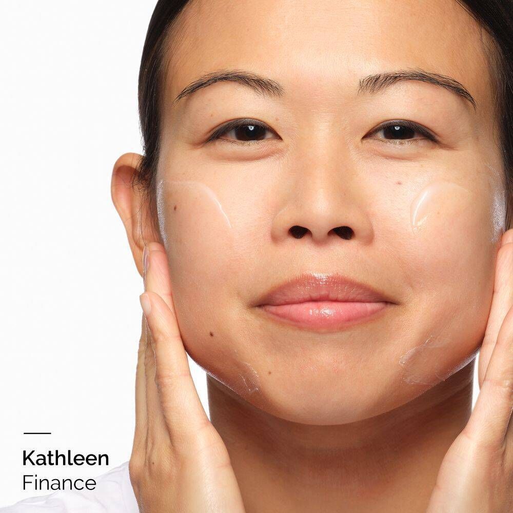 Nahaufnahme einer Person, die Creme auf ihr Gesicht aufträgt. Der Name 'Kathleen Finance' ist unten links zu sehen.