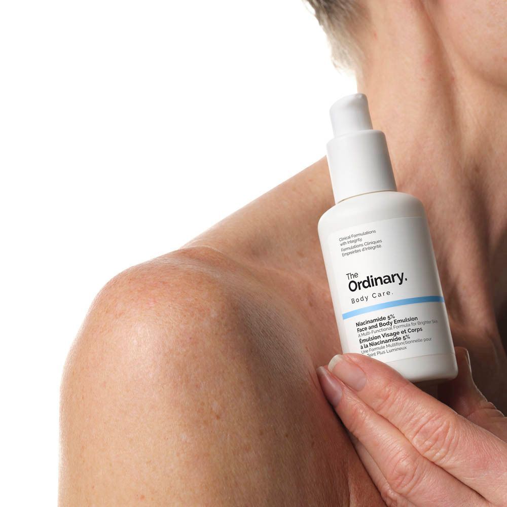 Person hält weiße Flasche The Ordinary Body Care. Aufschrift: Niacinamide 5% Face and Body Emulsion.