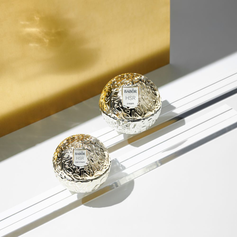 Zwei goldfarbene Cremetiegel mit Babor HSR cream auf Glasplatten. Hintergrund: gold.