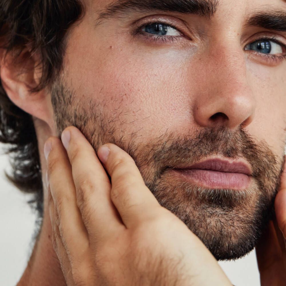 Gros plan d'un homme aux yeux bleus touchant ses joues.