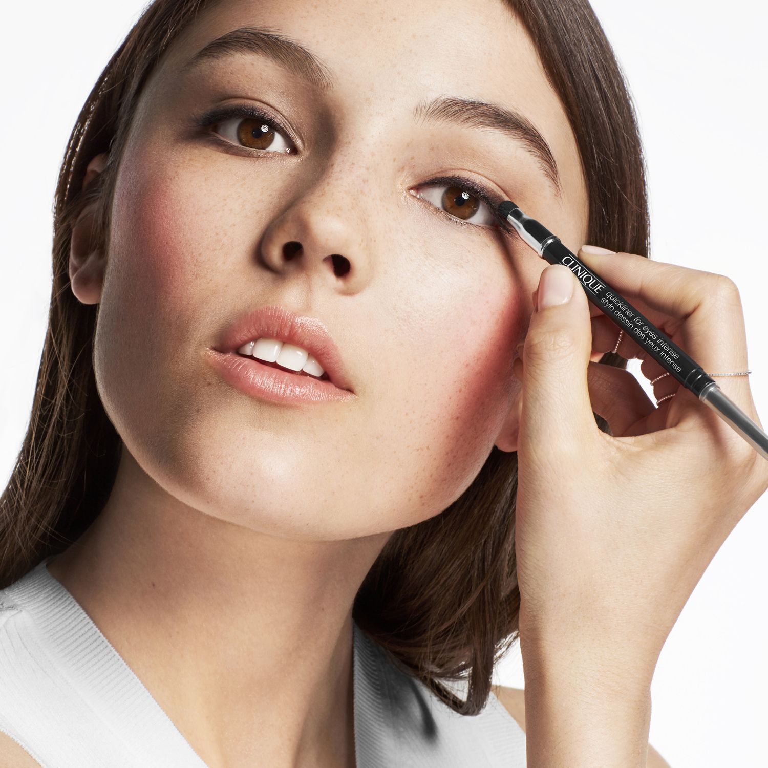 Eine junge Frau mit heller Haut, die sich mit einem Clinique Quickliner™ schwarz die Augen schminkt.