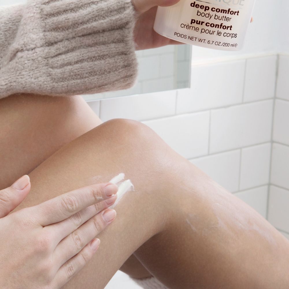Eine Hand trägt Clinique Deep Comfort Body Butter auf das Bein auf.