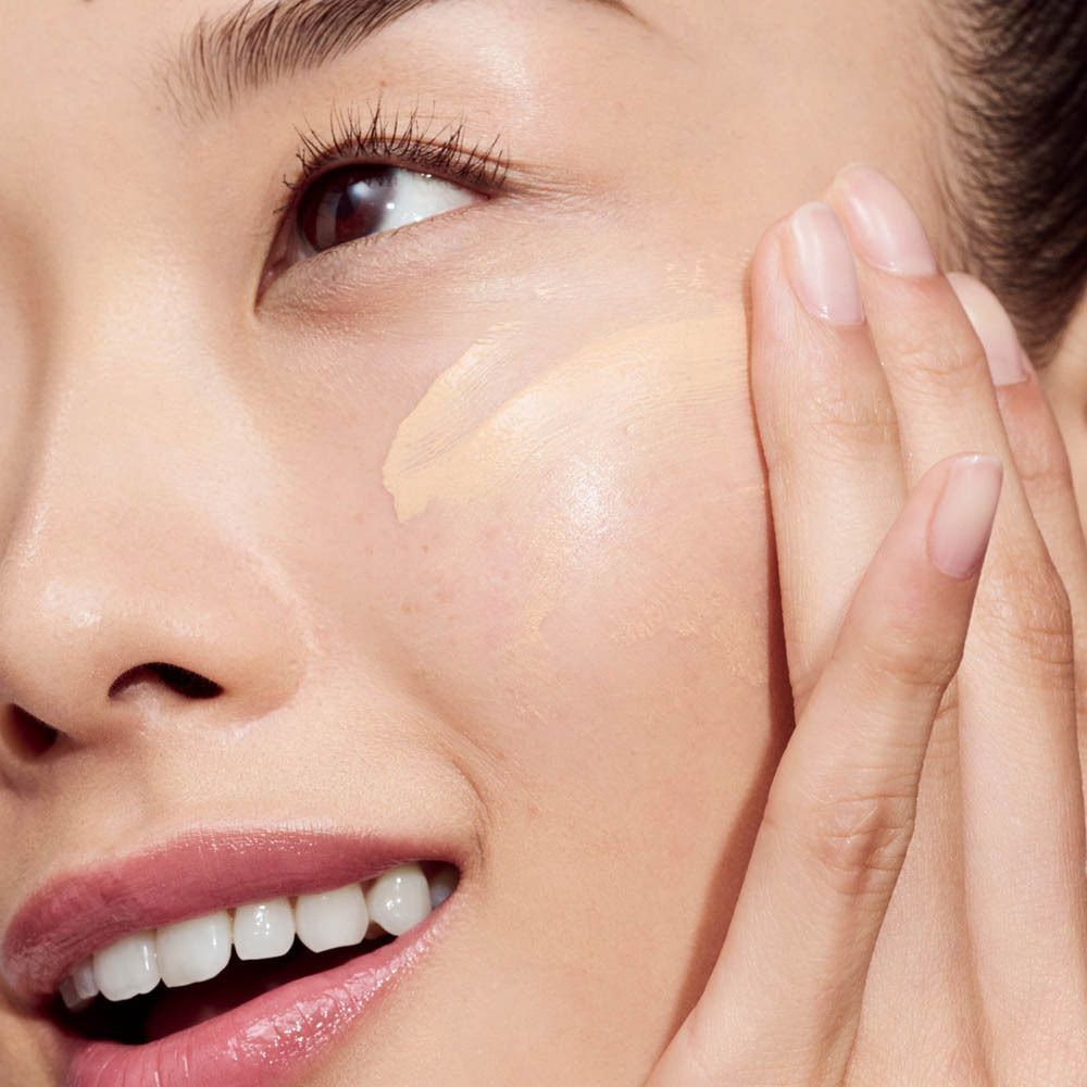 Nahaufnahme einer Frau, die Clinique Even Better Vitamin Makeup Light Cool 3 auf die Wange aufträgt.