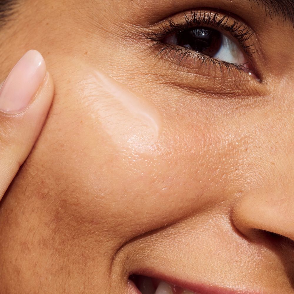 Eine Person trägt Clinique Even Better Clinical™ Serum auf die Wange auf.