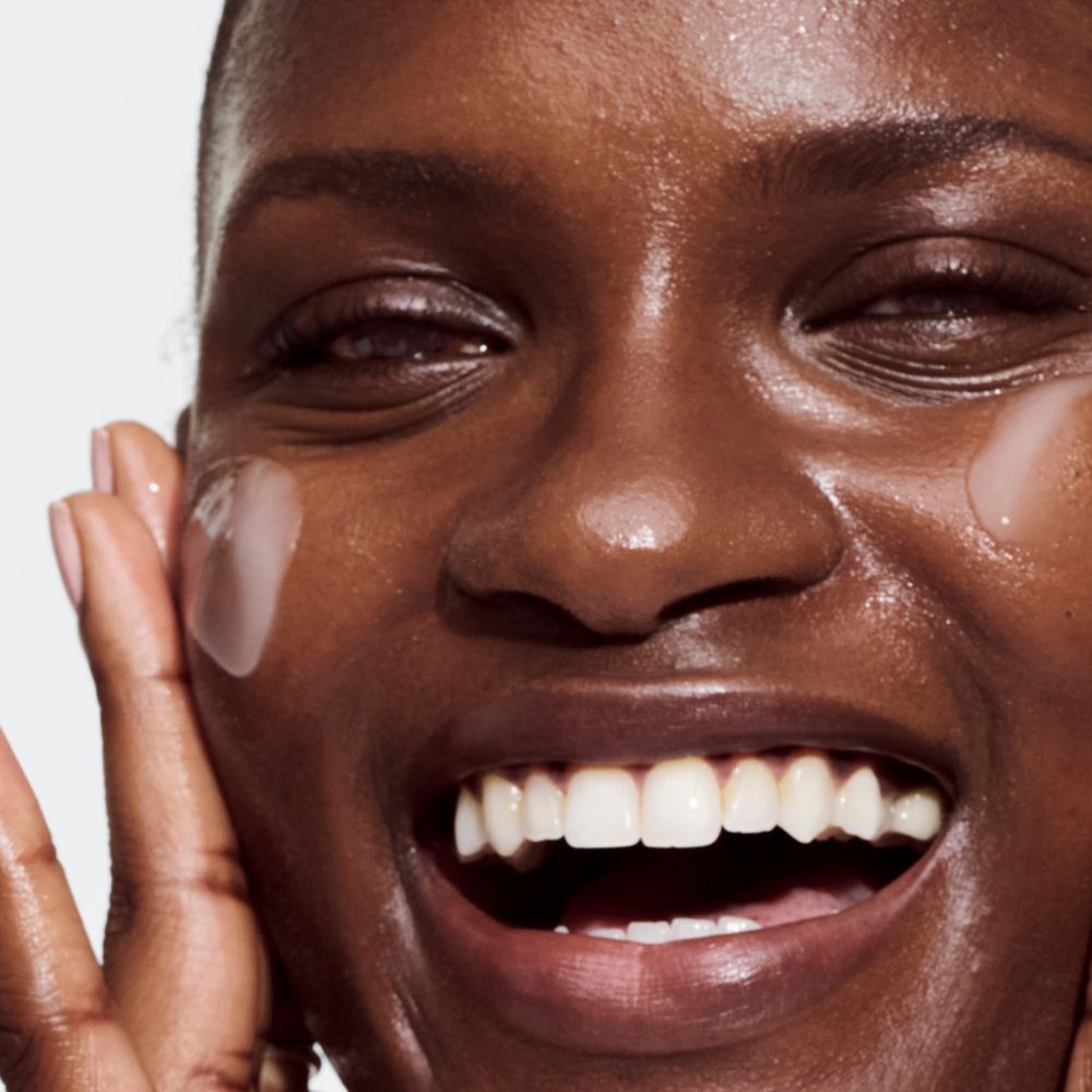 Eine Frau lacht, während sie Clinique Even Better Clinical™ Serum auf die Haut aufträgt.