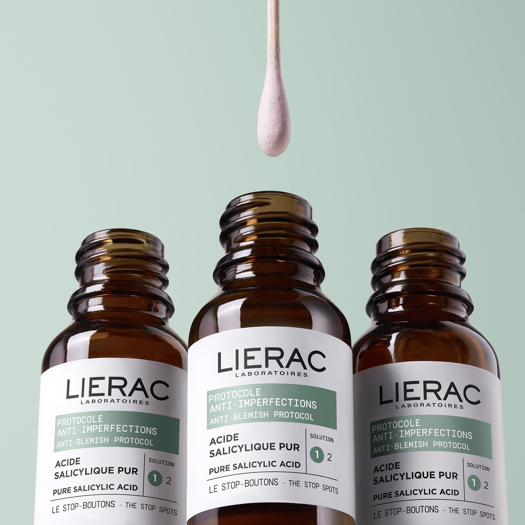 Drie bruine flessen met zwarte dop. Wattenstaafje met product. Merk: Lierac.
