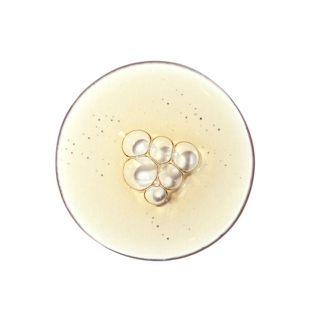 Tropfen der Lösung mit kleinen Bläschen und Glitzerpartikeln auf einer runden Oberfläche.