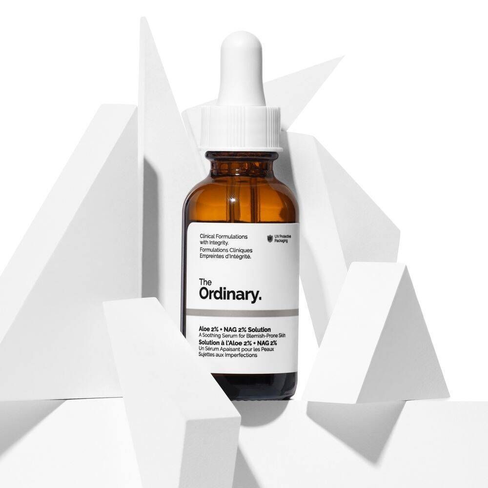 Eine Flasche 'The Ordinary Aloe 2% + NAG 2% Solution' mit Pipette, umgeben von weißen geometrischen Formen.