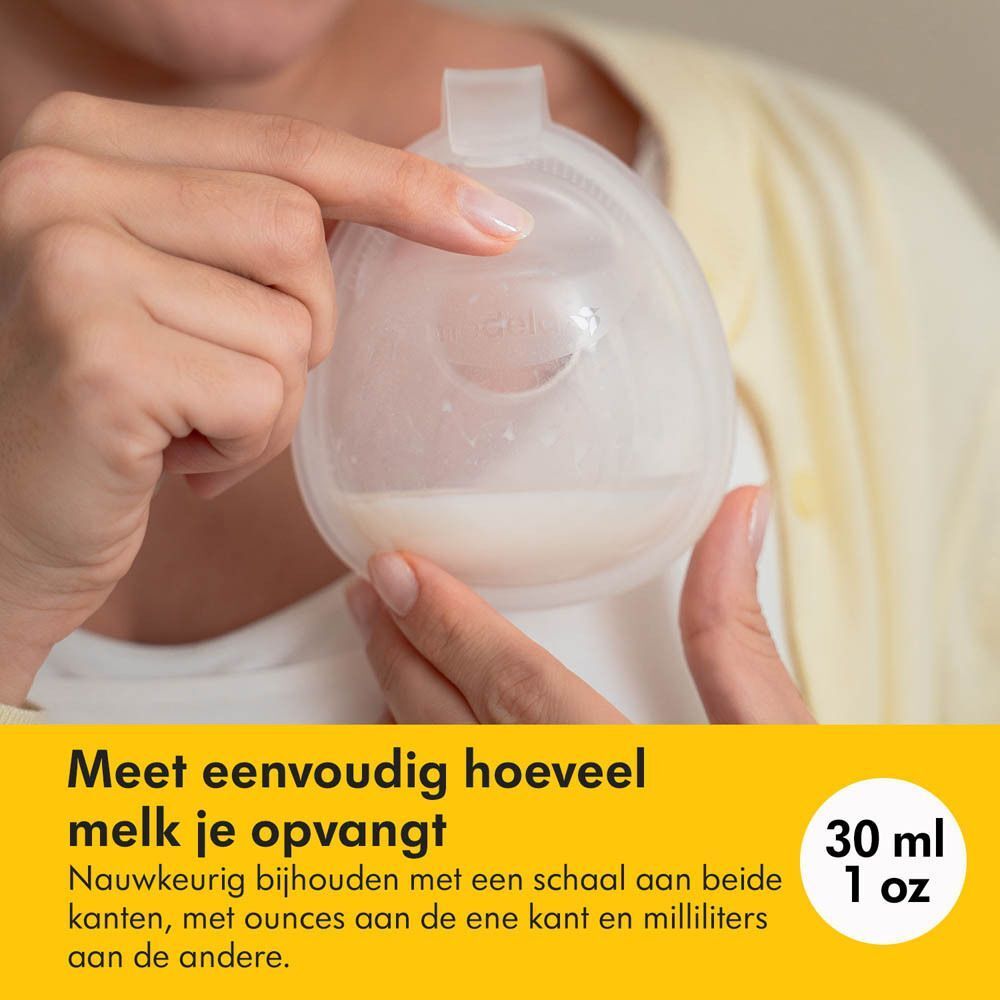 Een hand houdt een doorzichtige beker met moedermelk vast. De beker heeft een schaalverdeling in milliliters en ounces.