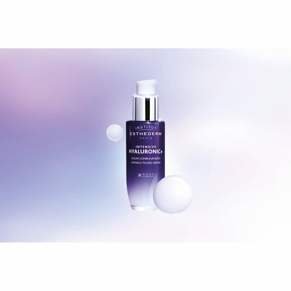 Flacon de sérum avec pompe argentée. Flacon bleu foncé. Inscription: Institut Esthederm, Intensive Hyaluronic+. Deux sphères blanches.
