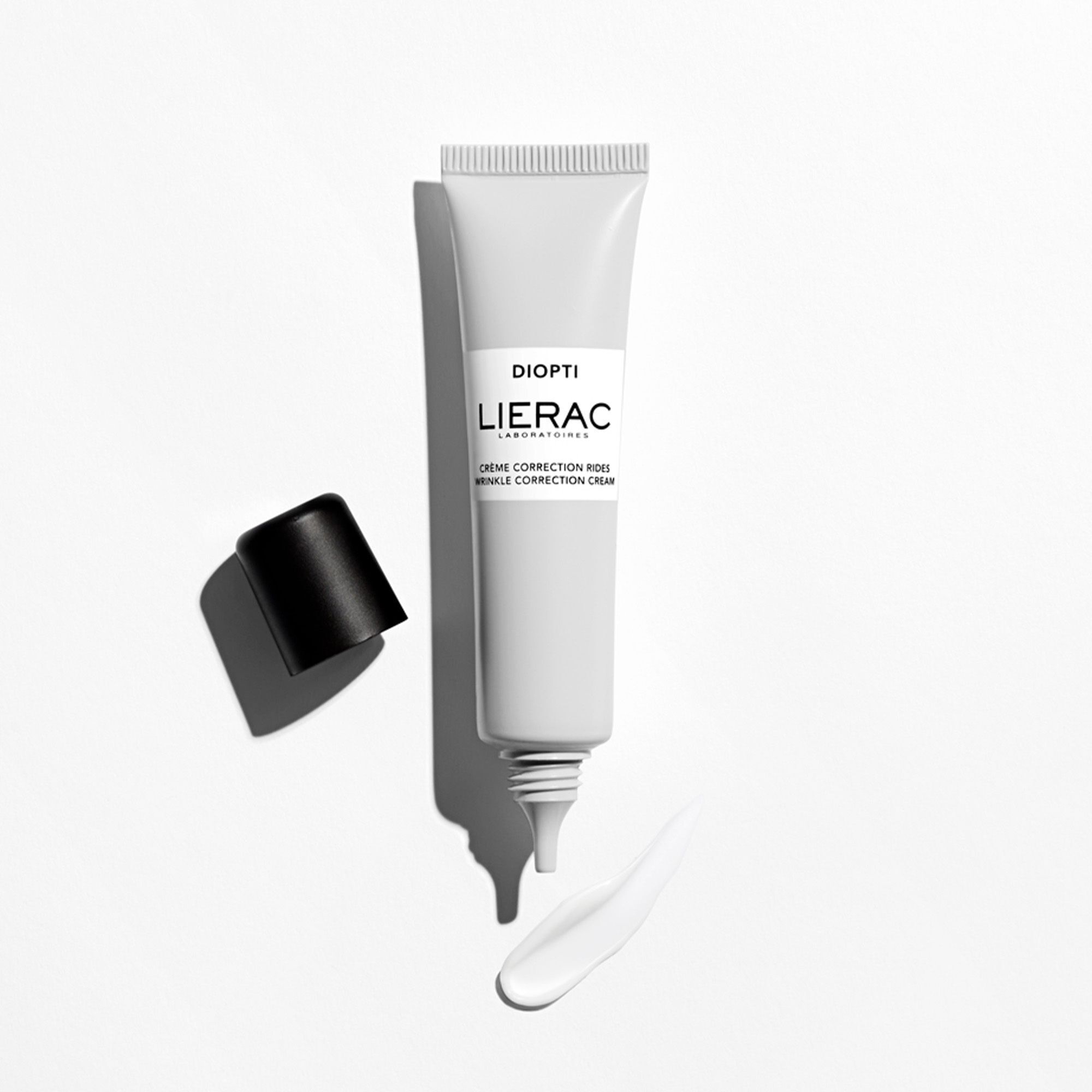 Lierac Diopti Crème Correction Rides tube, geopend. Zwarte dop ernaast. Streep crème. Tekst: Diopti, Lierac Laboratoires, Crème Correction Rides.