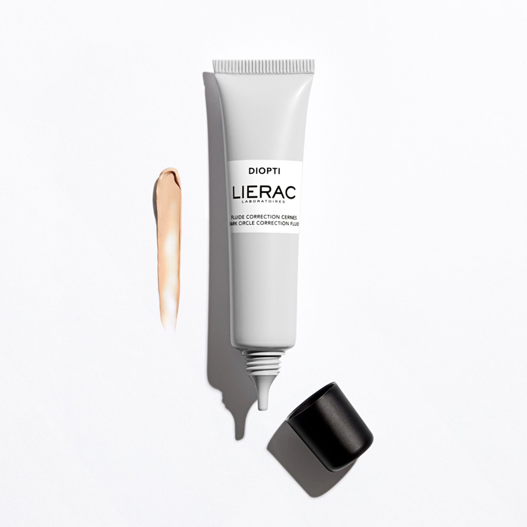 Tube gris avec bouchon noir et trace de produit. Inscription "DIOPTI", "LIERAC", et "FLUIDE CORRECTION CERNES" sur le tube.