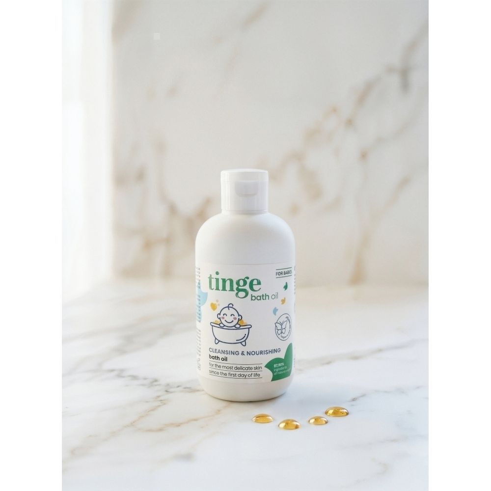 Bouteille blanche d'huile de bain Tinge, pour bébés, avec illustration d'un bébé souriant dans une baignoire.