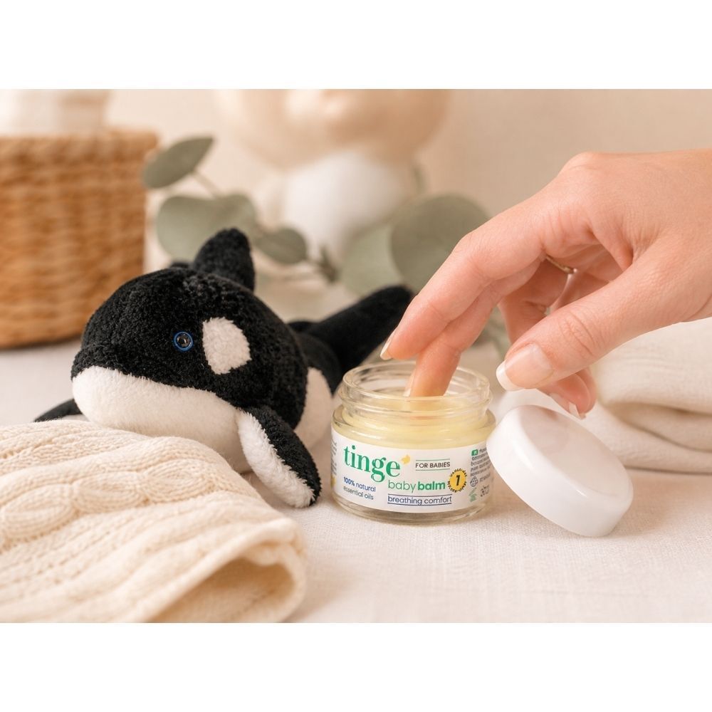 Hand die in Tinge Baby Balsem in een glazen pot duikt. Een knuffeldier ligt ernaast.