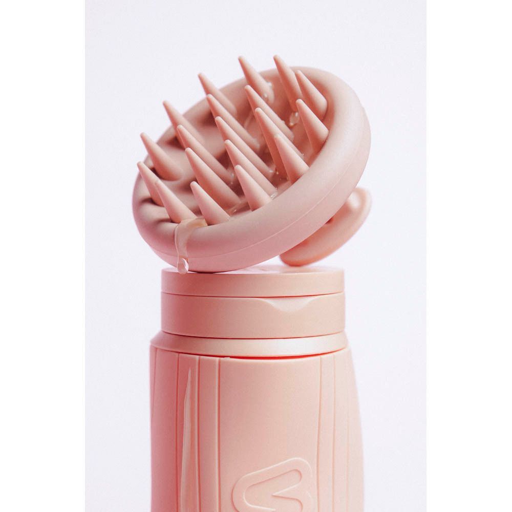 Een roze hoofdhuidmassager opzetstuk op een bijpassende fles met groeven.