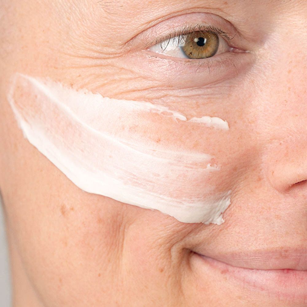 Een vrouw brengt een streep Gezichtsmasker Ultra-Réconfortant aan op haar wang.