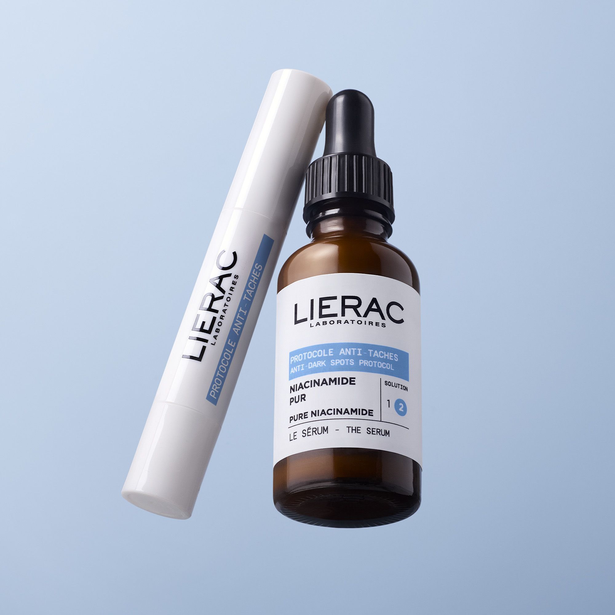 Flacon de sérum Lierac Anti-Taches et stylo, sur fond bleu.