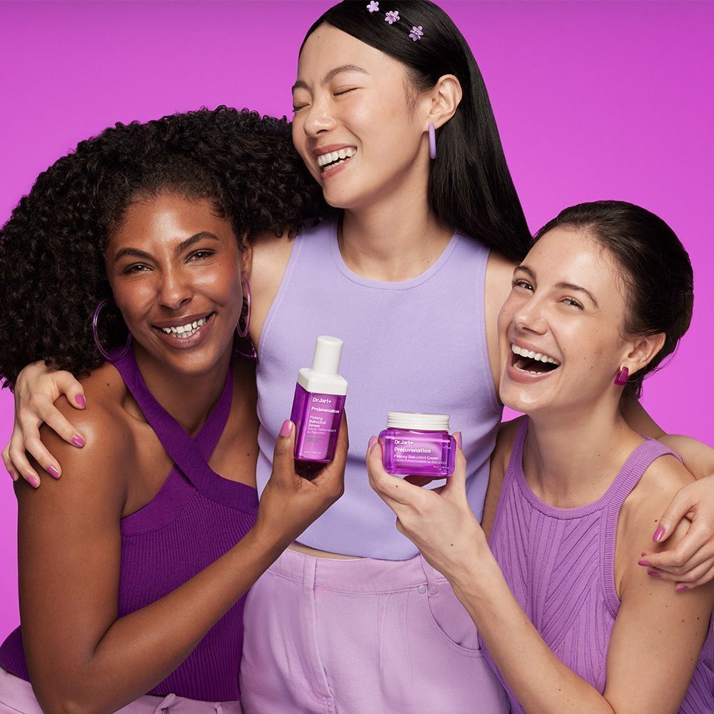 Drei lachende Frauen mit lila Kleidung und Kosmetikprodukten.