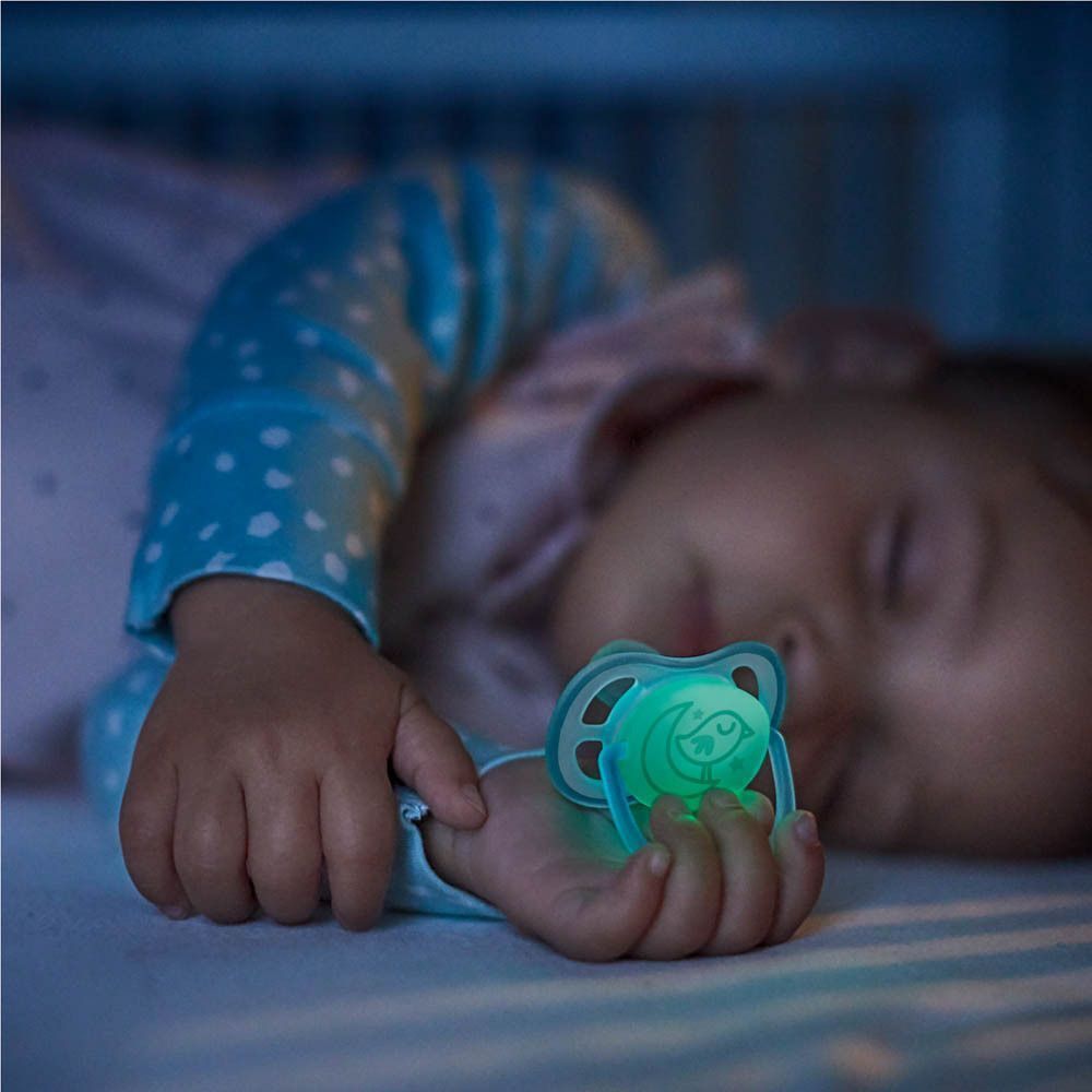 Un bébé dort avec une sucette phosphorescente dans la main.