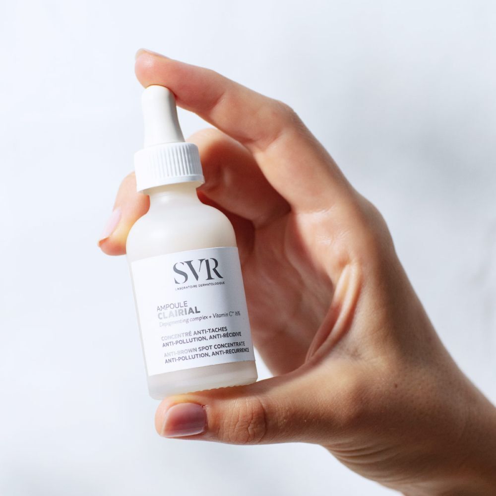 Hand die een SVR Ampoule Clairial flesje met druppelaar vasthoudt.