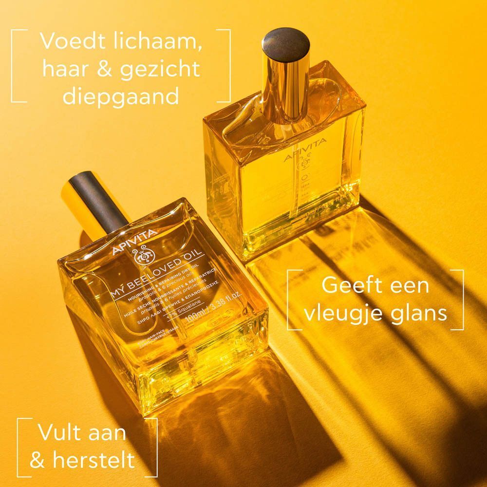 Een vrouw houdt een fles Apivita My Beeloved Oil vast, met vochtpercentages.