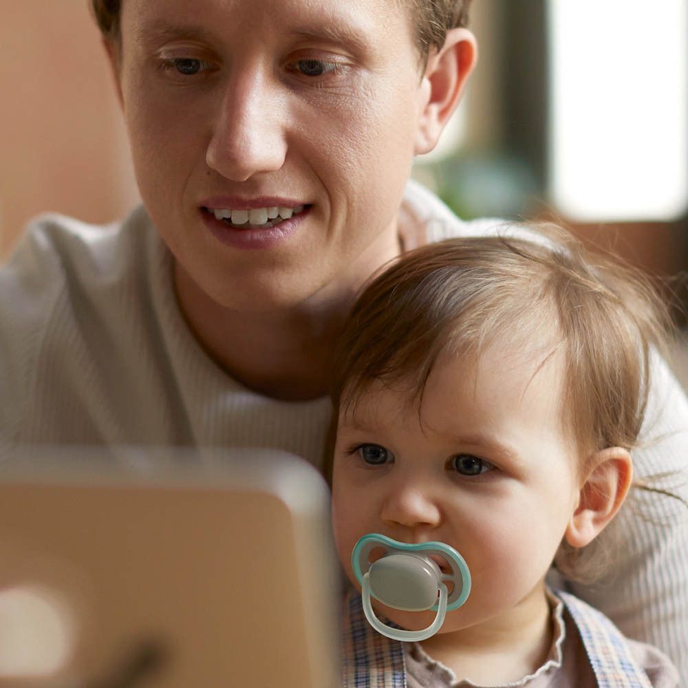 Bébé avec sucette, tenu par un homme regardant un ordinateur portable.