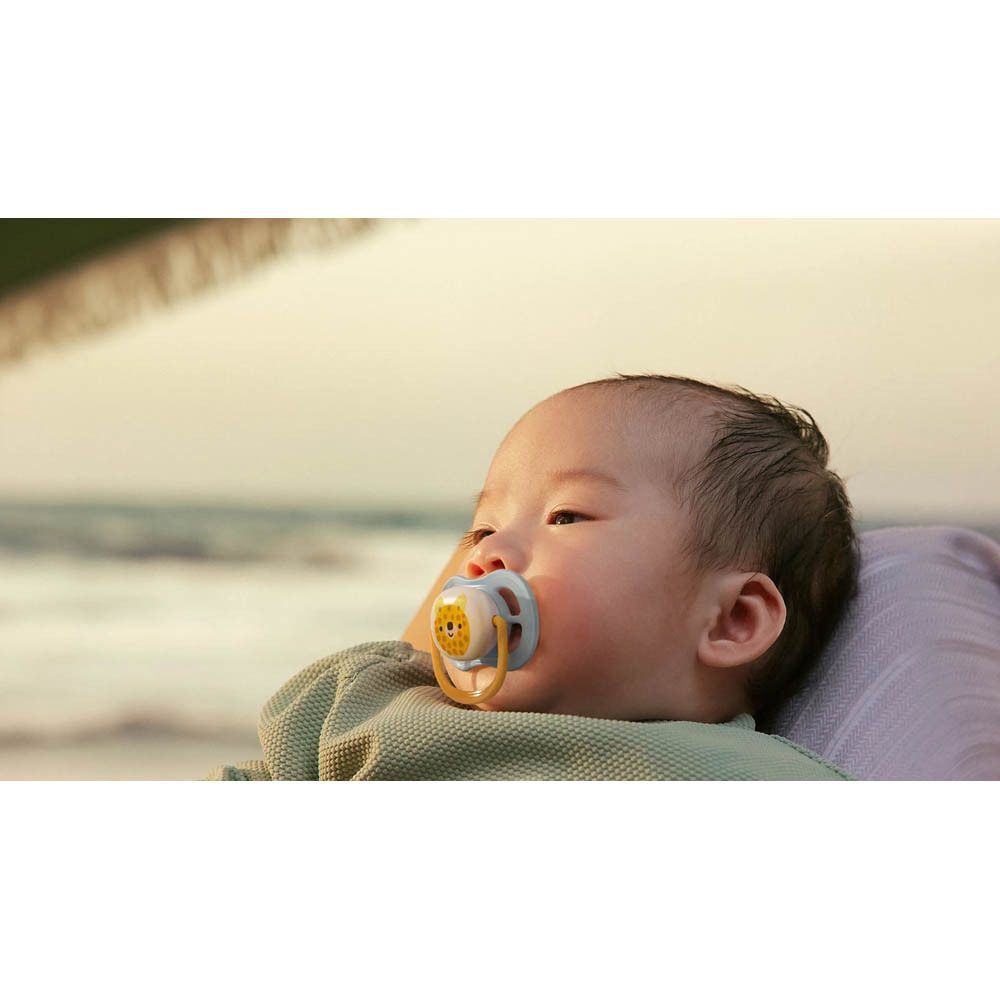 Une femme tenant un bébé sur la plage, avec une sucette dans la bouche.