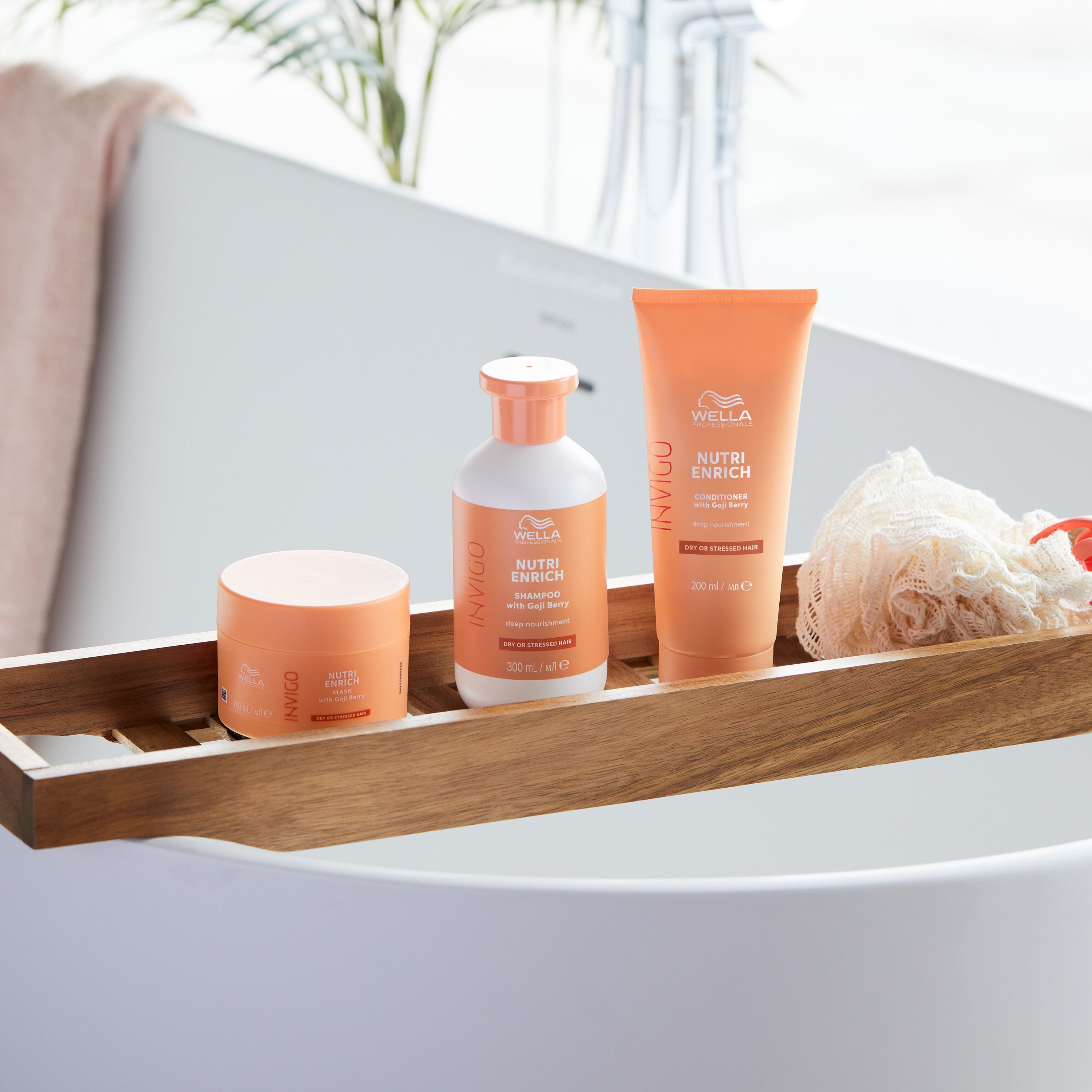 Trois produits capillaires Wella Nutri Enrich de couleur orange sur un plateau en bois dans une baignoire.