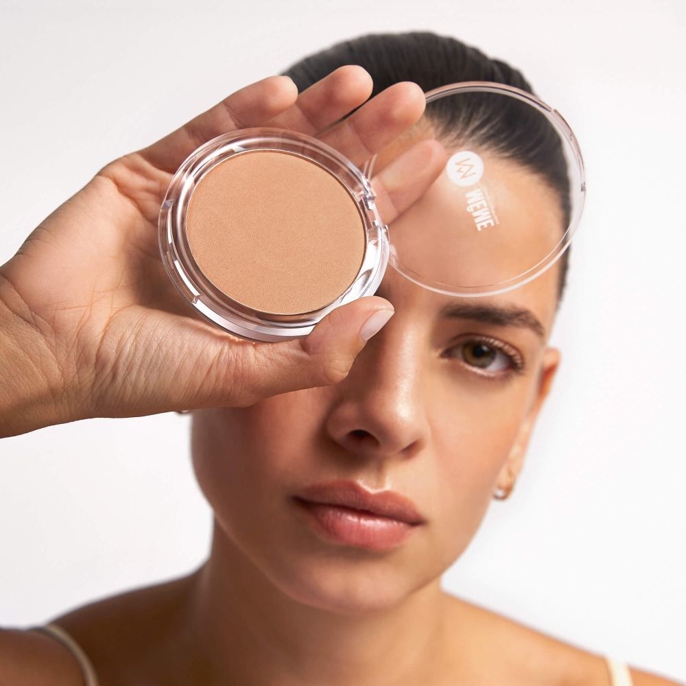 Een hand houdt een ronde verpakking met bronzing poeder voor het oog.