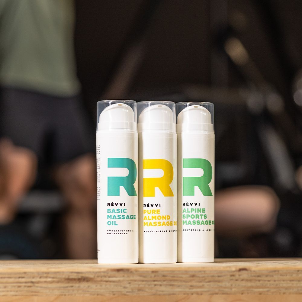 Trois flacons blancs avec distributeurs à pompe : huile de massage basique, huile de massage pure amande et huile de massage sportive alpine.