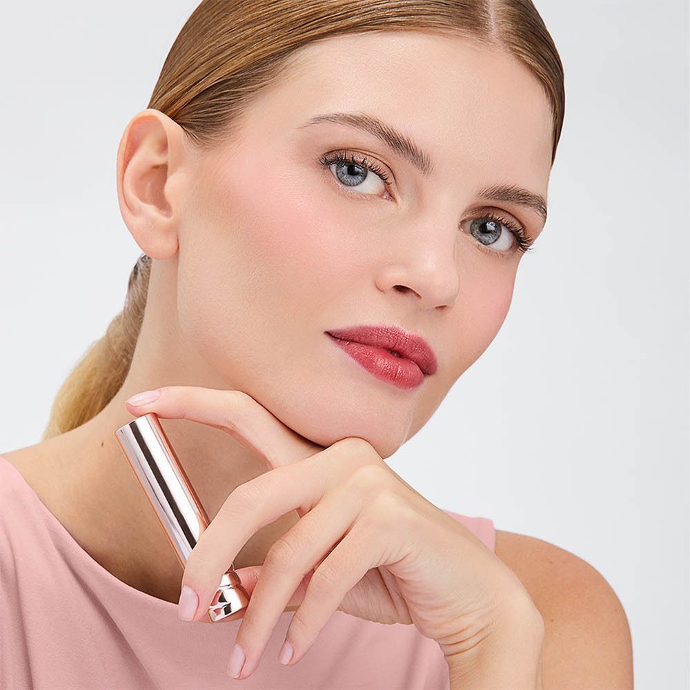 Een vrouw houdt een zilveren lippenstift vast. Ze draagt roze kleding en rode lippenstift.