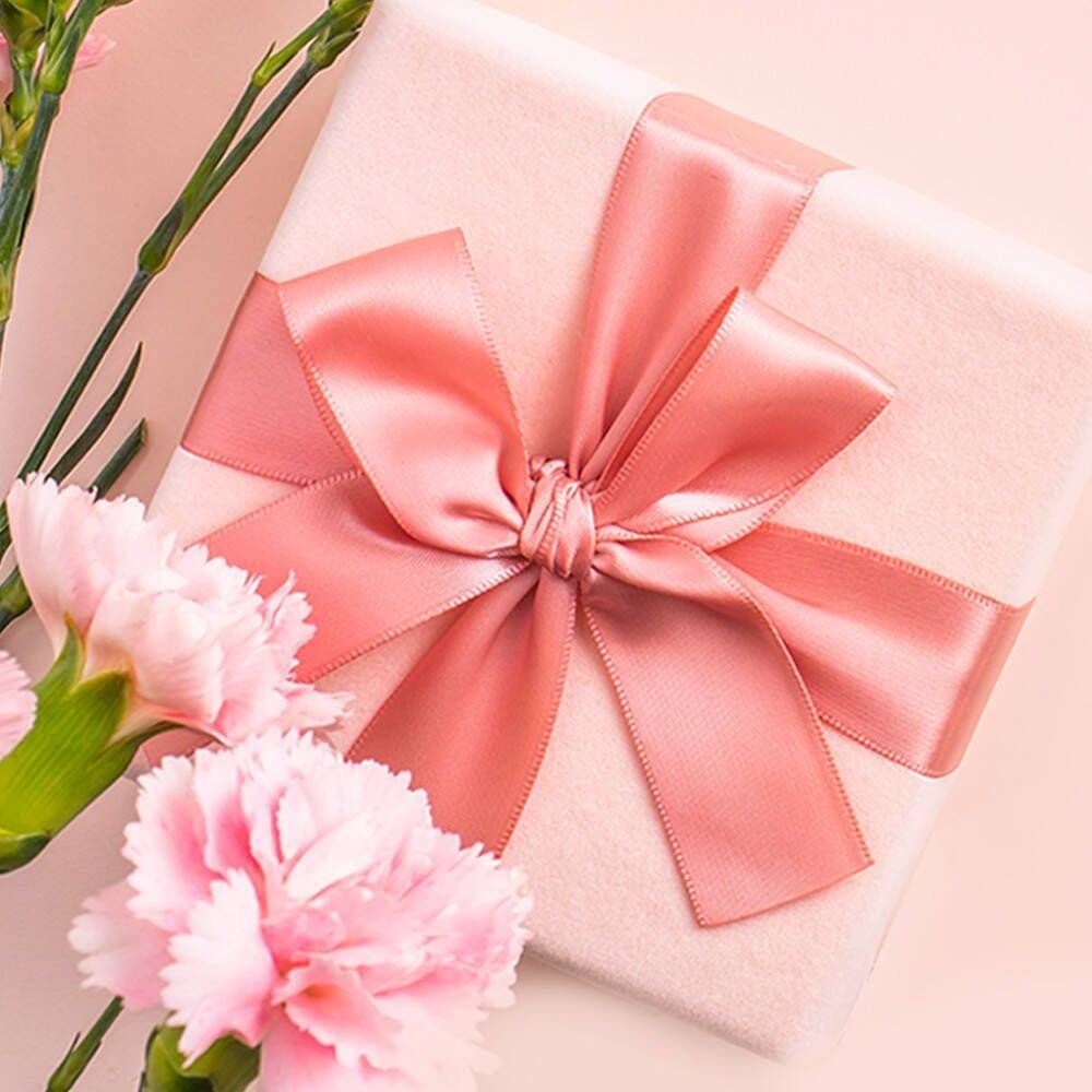 Scatola regalo rosa con fiocco e garofani. La scatola è legata con un nastro rosa. Accanto ci sono dei garofani rosa.