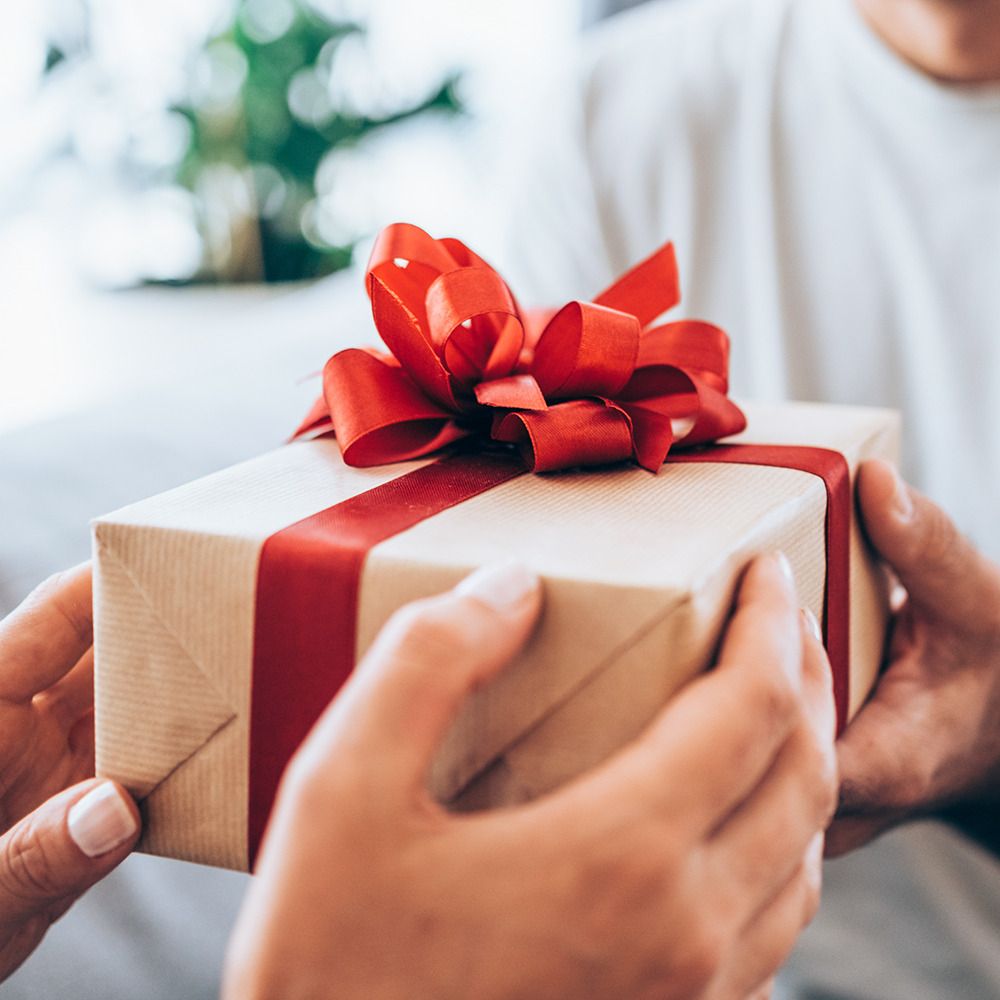 Boîte cadeau avec ruban et nœud rouge. Mains tenant la boîte. Papier brun, nœud rouge.