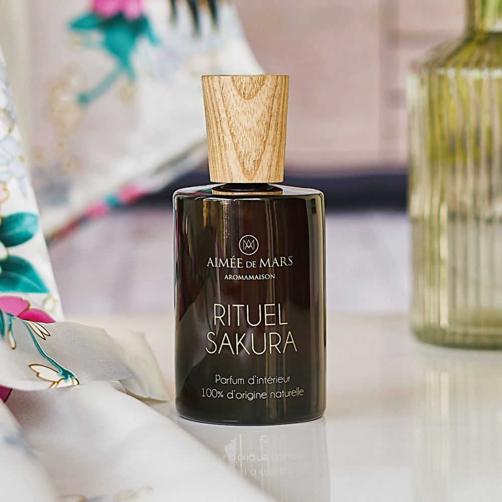 Braune Glasflasche mit Holzverschluss. Aufschrift: RITUEL SAKURA, Parfum d'intérieur, 100% d'origine naturelle. Auf Tisch.