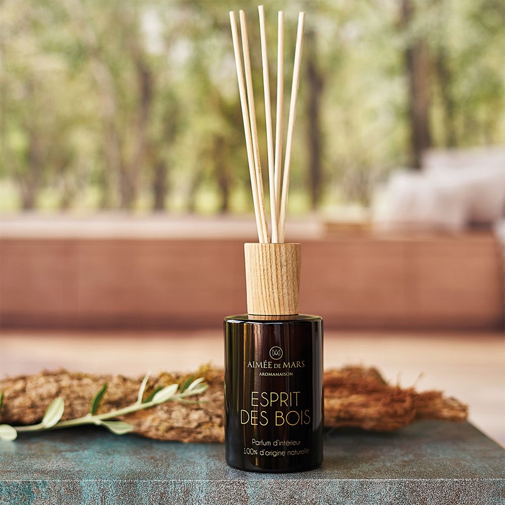 Braune Glasflasche mit Holzverschluss und Duftstäbchen. Produktname: Esprit des Bois. Hintergrund: verschwommene Natur.