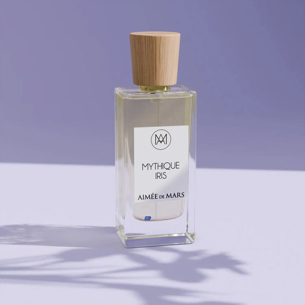 Parfümflakon mit Holzverschluss. Aufschrift: Mythique Iris, Aimée de Mars. Rechteckige Glasflasche auf lila Hintergrund.