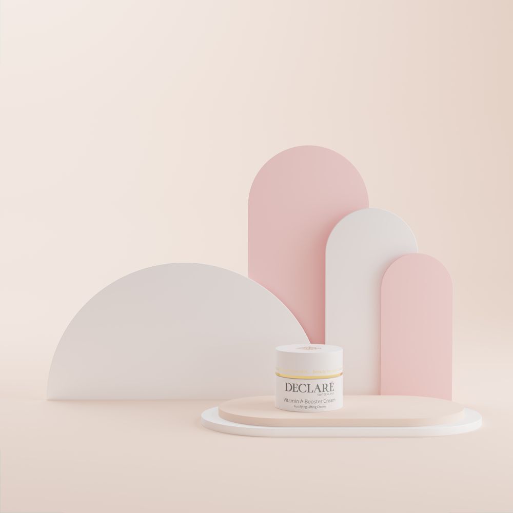 Weißes Tiegel auf Podest. Hintergrund mit weißen und rosa Formen. DECLARÉ Vitamin A Booster Cream.