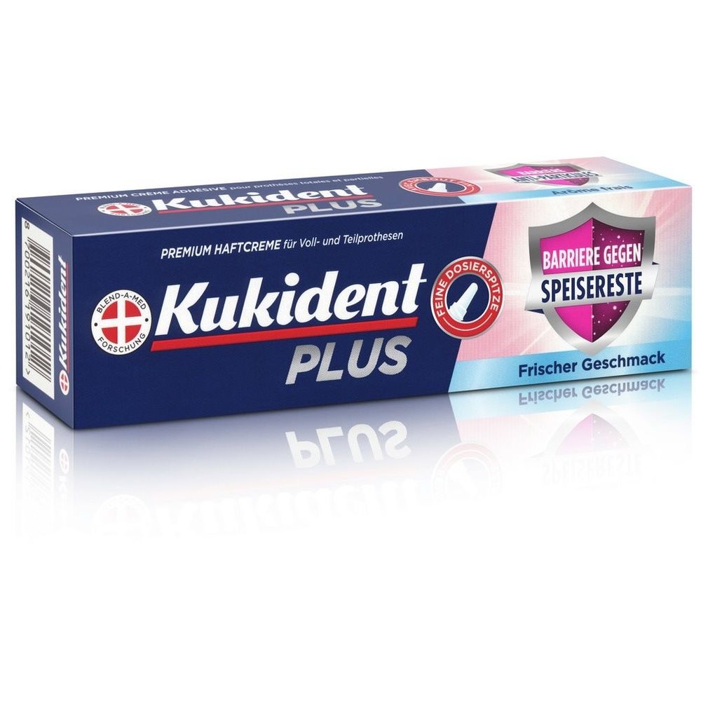 Emballage de Kukident Plus Premium. Boîte bleue avec nom et logo du produit. Texte : Barrière contre les restes alimentaires, goût frais.