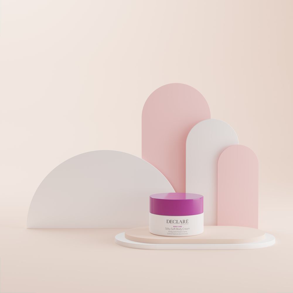 Weißer Tiegel mit lila Deckel auf Podest. Dekorative Formen in Rosa und Weiß im Hintergrund. DECLARÉ-Logo sichtbar.