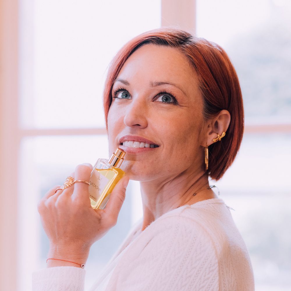 Frau hält Aimée de Mars Natasha Eau de Parfum Flakon. Sie lächelt und hält den Flakon nah am Gesicht.