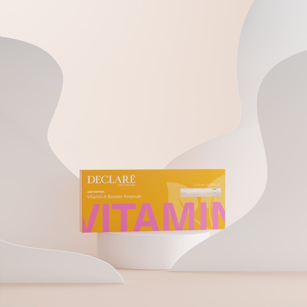 Gelbe Schachtel DECLARÉ Vitamin A Booster Ampulle auf Podest. Rosa Schriftzug "VITAMIN". Hintergrund mit Formen.